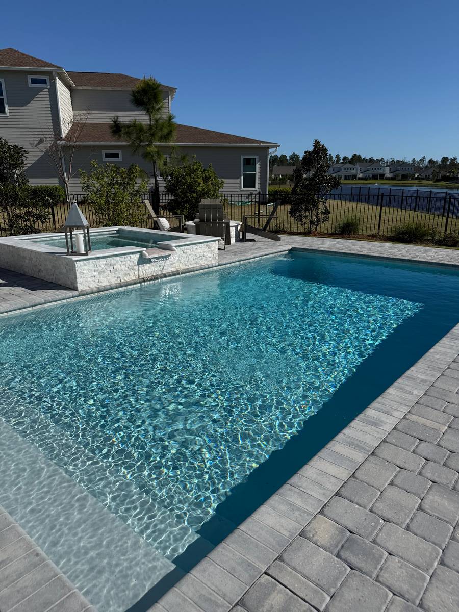 Sparkling clear pool with a raised stone spa and spillover, paver deck and a lake view