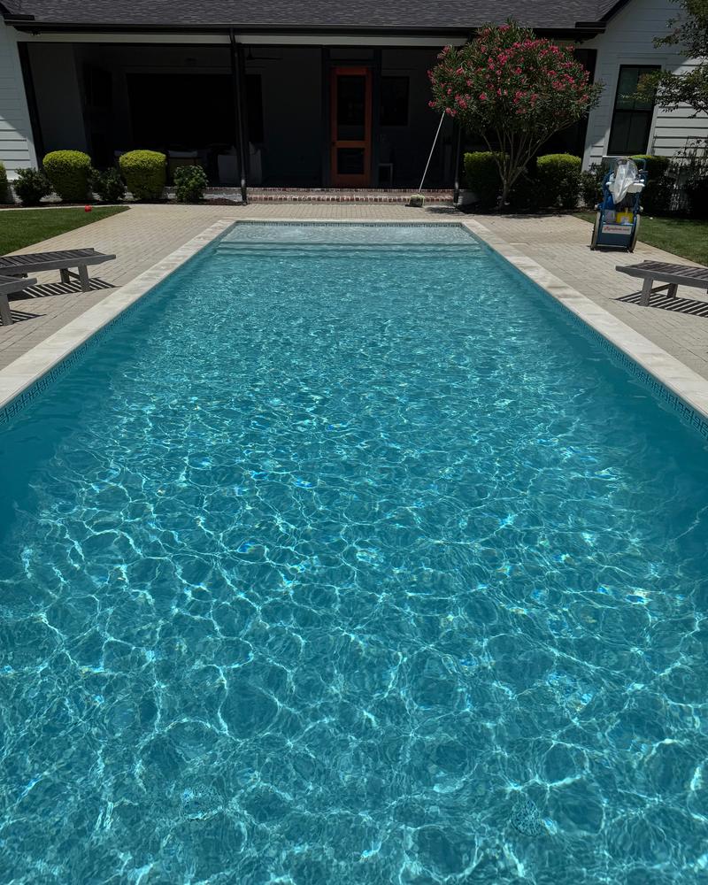 Long rectangular pool with sparkling blue water in front of a white home