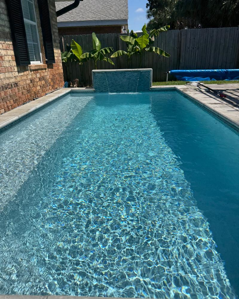 Long blue pool with a tiled water wall and tropical plants